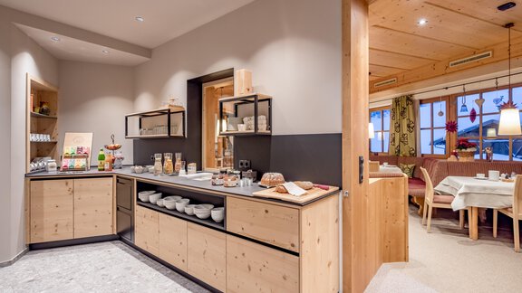 A modern kitchen with wooden shelves and a selection of food. In the background, a cozy dining area is visible. - Hotel-Garni Pirchhütt - Obergurgl 