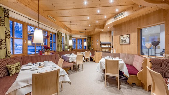 A cozy restaurant with wooden decor and warm lighting. Tables are carefully set and provide space for guests. - Hotel-Garni Pirchhütt - Obergurgl 