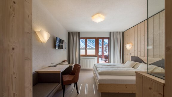 A modern hotel room with two beds, a desk, and a comfortable seating area. Large windows offer a view of the mountains. - Hotel-Garni Pirchhütt - Obergurgl 