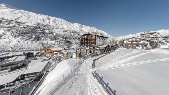 A snowy mountain landscape with a small village. In the background, there are high mountains and a blue sky. - Hotel Gotthard-Zeit - Obergurgl 