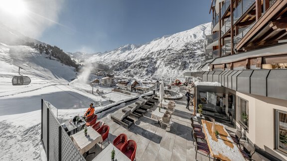 A beautiful view of an alpine landscape with snow-capped mountains. In the foreground, you can see cozy seating areas and a cable car that opens up the mountainous world. - Hotel Gotthard-Zeit - Obergurgl 