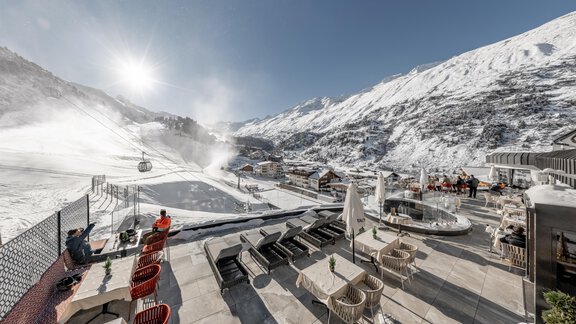 A mountain landscape full of snow with a clear blue sky. In the foreground, there are lounges and seating on a terrace. - Hotel Gotthard-Zeit - Obergurgl 