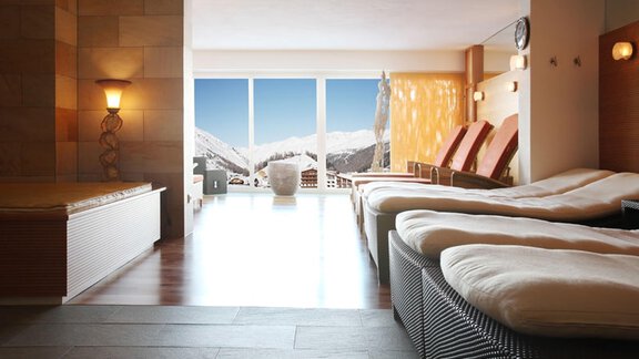 A cozy wellness area with loungers and large windows. The view shows snow-covered mountains and a clear sky. - Hotel Olympia - Obergurgl 