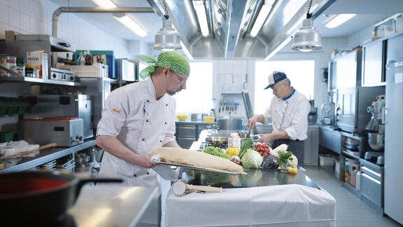 Two chefs are working in a modern kitchen. One is preparing dough while the other is cutting fresh vegetables. - Hotel Olympia - Obergurgl 