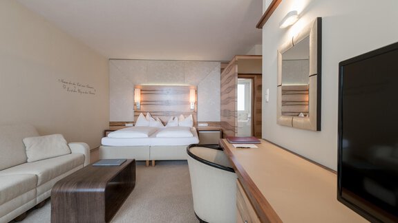 A modern room with two beds, a sofa, and a table. The bright decor creates an inviting atmosphere. - Hotel Olympia - Obergurgl 