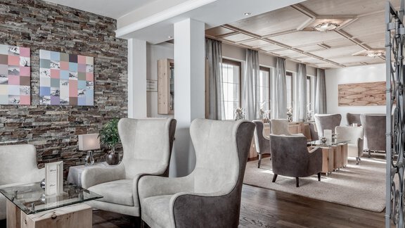 An elegant living space with modern armchairs and a stylish wooden floor. The walls are decorated with stone and artwork, creating a cozy atmosphere. - Hotel Olympia - Obergurgl 