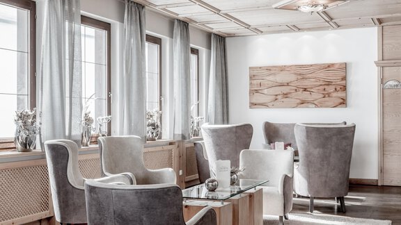 An elegant lounge area with modern gray armchairs and a wooden table. Large windows let in plenty of light and create an inviting atmosphere. - Hotel Olympia - Obergurgl 