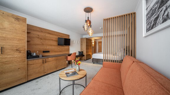 A modern room with an orange sofa and wooden furniture.  
On the wall, there is a television, and a stylish table complements the decor. - Hotel Olympia - Obergurgl 