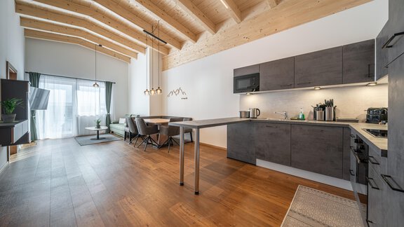 A modern kitchen with wooden ceilings and an open living area. The room has large windows that let in plenty of light. - Mein Gaisberg - Obergurgl 