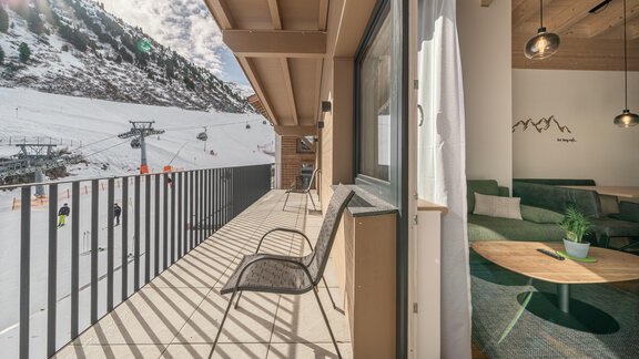 A cozy balcony with chairs that offers a view of a snowy mountain landscape and ski lifts. Inside, there is a modern living room with an inviting atmosphere. - Mein Gaisberg - Obergurgl 