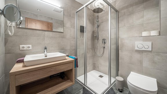 A modern bathroom with a glass shower cubicle and a wooden sink. The walls are painted in neutral gray tones. - Mein Gaisberg - Obergurgl 