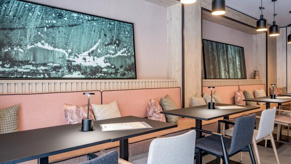 A modern restaurant with minimalist decor. The tables are black and surrounded by comfortable, light-colored chairs, while the walls are decorated with artistic paintings. - The Moss - Your unique hideaway - Obergurgl 