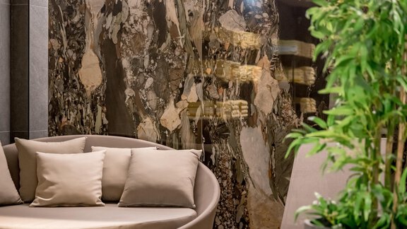 An elegant seating area with a round sofa and cushions. In the background, a stylish wall with a unique stone pattern is visible. - The Moss - Your unique hideaway - Obergurgl 