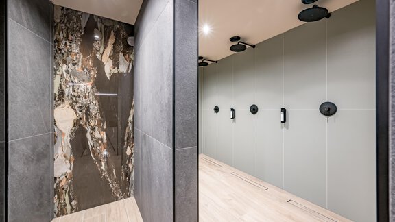 A modern bathroom with dark walls and elegant partitions. On the right side, there are showers with minimalist fixtures. - The Moss - Your unique hideaway - Obergurgl 