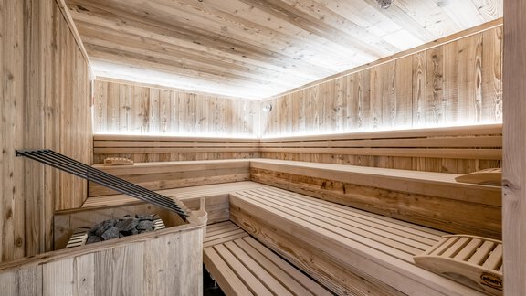 A modern sauna made of light wood with bench-like seating areas. Soft light creates a relaxing atmosphere. - The Moss - Your unique hideaway - Obergurgl 