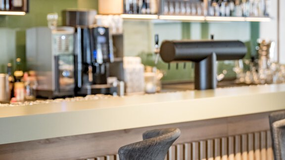 A modern bar with stylish bar stools and a lit shelf. Various alcoholic beverages are ready behind the counter. - The Moss - Your unique hideaway - Obergurgl 