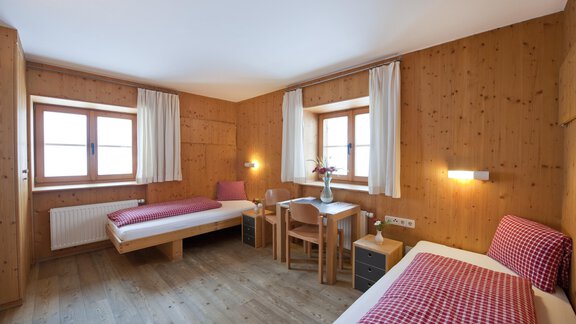 A cozy room with two beds and wooden paneling. There is a small table and windows with a view. - Universitätszentrum Obergurgl - Obergurgl 