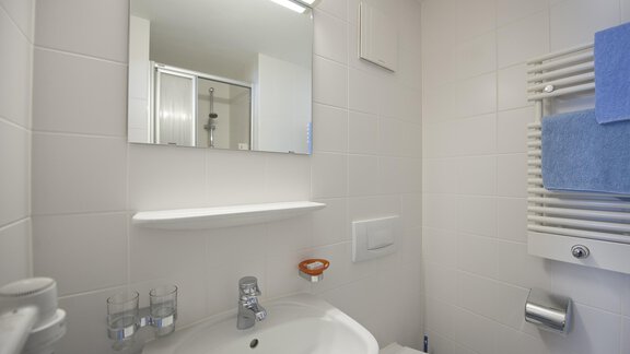 A small bathroom with a white sink and a mirror. The walls are tiled in light colors and there are towels in blue. - Universitätszentrum Obergurgl - Obergurgl 
