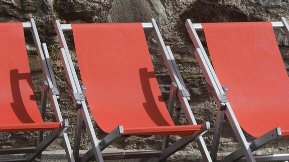 Red loungers are lined up against a stone wall. They are ready for relaxing hours outdoors. - Universitätszentrum Obergurgl - Obergurgl 