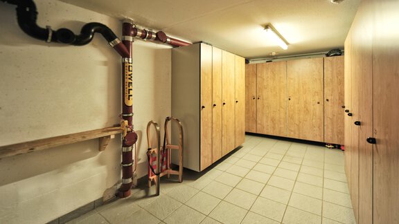A functional space with gray tiled floor and wooden cabinets. Pipes are visible on the wall, which are part of the technical equipment. - Haus Timmelseck - Obergurgl 