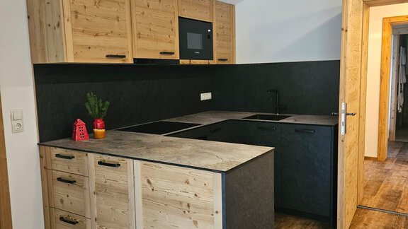 Eine moderne Küche mit hellen Holzmöbeln und schwarzer Arbeitsfläche. Der Raum ist gut beleuchtet und hat einen gemütlichen Holzfußboden. - Almhof Mareil - Ochsengarten