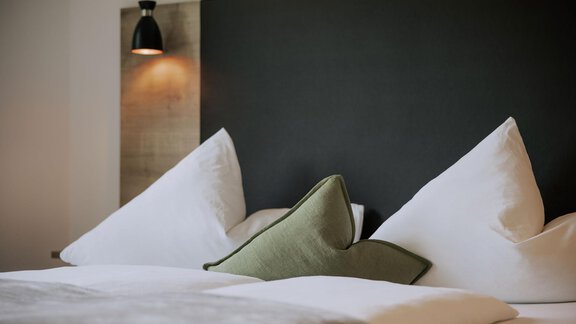 Ein modernes Schlafzimmer mit einem großen Bett und eleganten Kissen. Die dunkle Wand und die sanfte Beleuchtung schaffen eine gemütliche Atmosphäre. - Apartment Waldesruh - Ochsengarten