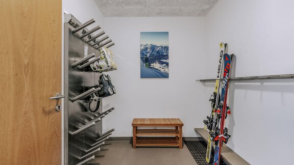 Ein Raum zum Skilager mit Skiern und einem Holzbank. An der Wand hängt ein Bild von einer Berglandschaft. - Apartment Waldesruh - Ochsengarten