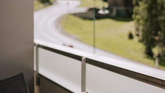 Ein Balkon mit einem Holztisch und einem Blick auf eine grüne Landschaft. Im Hintergrund sind Bäume und einige Gebäude sichtbar. - Apartment Waldesruh - Ochsengarten