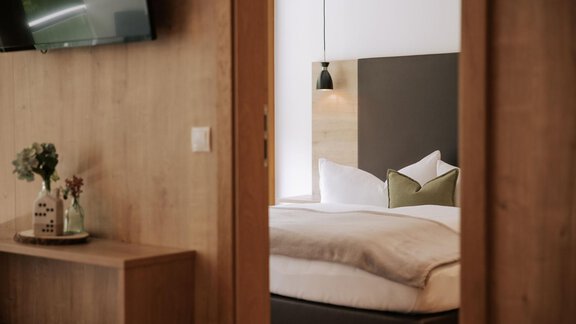 Ein gemütliches Schlafzimmer mit einem großen Bett und modernen Kissen. Im Hintergrund sind ein Holzregal und ein TV-Gerät zu sehen. - Apartment Waldesruh - Ochsengarten
