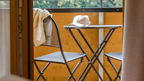 Ein kleiner Balkon mit zwei Klappstühlen und einem runden Tisch. Im Hintergrund sind grüne Bäume zu sehen. - Gasthof Waldesruh - Ochsengarten