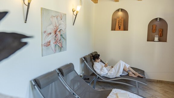 Ein entspannender Wellnessbereich mit Liegen und sanfter Beleuchtung. Eine Person in einem Bademantel genießt ihre Auszeit. - Gasthof Waldesruh - Ochsengarten