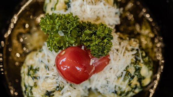 Eine Portion Spinatknödel mit Parmesan, garniert mit Petersilie und Cherry-Tomate. Die Knödel liegen in einer dunklen Schale. - Gasthof Waldesruh - Ochsengarten