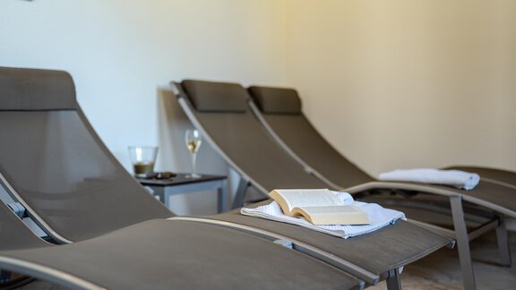 Ein entspannender Bereich mit Liegen und einem Tisch. Auf dem Tisch liegen ein Buch und ein Glas Wasser. - Gasthof Waldesruh - Ochsengarten