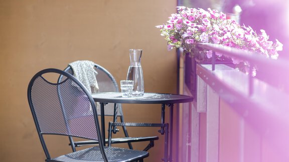 Ein gemütlicher Balkon mit einem kleinen Tisch und zwei Stühlen. Blumen schmücken das Geländer und ein Glas Wasser steht bereit. - Gasthof Waldesruh - Ochsengarten