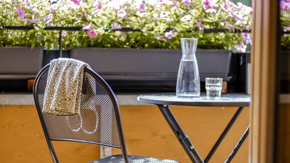 Ein kleiner Tisch mit einem Stuhl auf einem Balkon. Im Hintergrund blühen pinke Blumen und es gibt eine Karaffe mit Wasser. - Gasthof Waldesruh - Ochsengarten