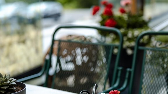 Ein schön angerichtetes Dessert in einer kleinen Pfanne, dekoriert mit roten Beeren. Im Hintergrund sind Pflanzen und eine Terrasse mit Blick auf die Natur zu sehen. - Gasthof Waldesruh - Ochsengarten