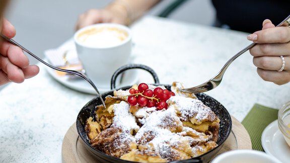 Ein köstliches Gericht in einer Pfanne, garniert mit Puderzucker und roten Beeren. Dazu stehen zwei Tassen Kaffee auf einem Tisch. - Gasthof Waldesruh - Ochsengarten