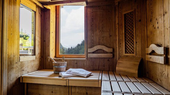 Eine helle Sauna aus Holz mit großen Fenstern und Blick auf die Natur. Im Inneren sind Holzliegen und ein Eimer mit Handtuch zur Entspannung vorhanden. - Gasthof Waldesruh - Ochsengarten