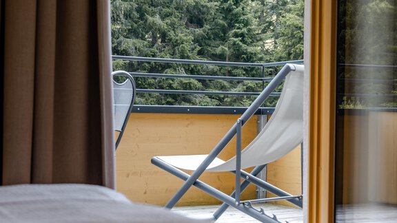 Ein gemütliches Zimmer mit Blick auf einen Balkon. Draußen sind grüne Bäume und eine Liege. - Gasthof Waldesruh - Ochsengarten
