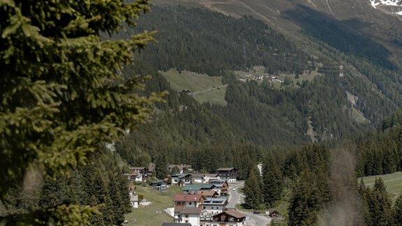 Ein malerisches Dorf in den Bergen, umgeben von grünen Wäldern und hohen Gipfeln. Die Straße schlängelt sich durch die Landschaft in Richtung des Dorfes. - Gasthof Waldesruh - Ochsengarten