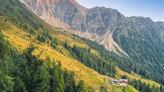 A picturesque mountain landscape with green meadows and dense forests. In the background, majestic mountains with a red peak are visible. - Acherberg Alm - Oetz