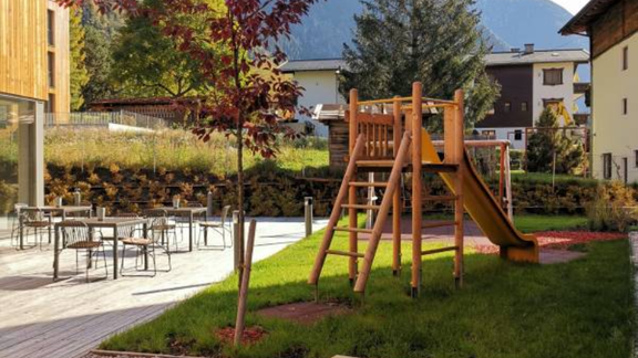 A beautiful playground with a slide and a sandbox. In the background, mountains and a green landscape can be seen. - All-Suite Resort Ötztal - Oetz