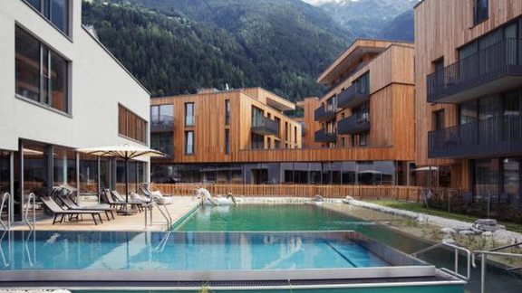 A modern accommodation with wooden elements and a swimming pool. In the background, green mountains can be seen. - All-Suite Resort Ötztal - Oetz