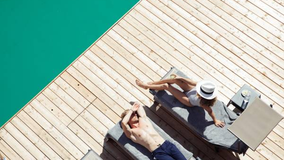 A couple relaxes on loungers by a pool. The sun is shining as they unwind and enjoy drinks. - All-Suite Resort Ötztal - Oetz