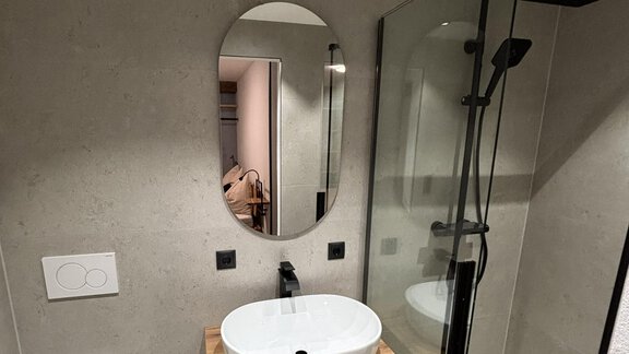 A modern bathroom with a glass shower and a stylish sink. The walls are made of gray concrete, and there is a round mirror. - ALPENBLICK de Luxe - Oetz