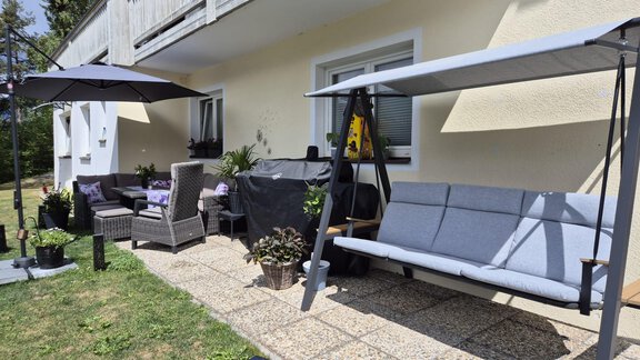 Ein gemütlicher Außenbereich mit einer Hollywoodschauckel, Sitzgelegenheiten und einem Sonnenschirm. Die Terrasse ist von Pflanzen umgeben und bietet einen einladenden Platz zum Entspannen. - Alpenlove - Oetz