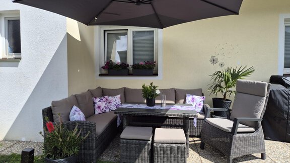 Eine gemütliche Sitzecke im Freien mit einem großen Sonnenschirm. Der Bereich ist mit Pflanzen und Kissen dekoriert, ideal zum Entspannen. - Alpenlove - Oetz