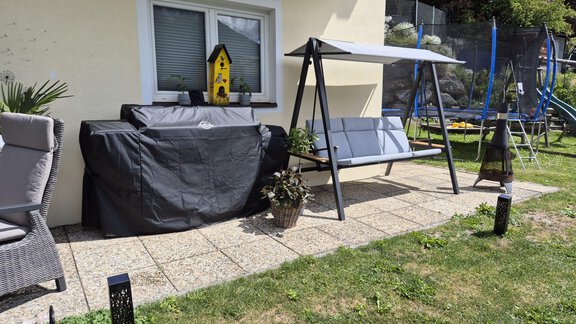 Ein gemütlicher Garten mit Sitzecke, einem Grill und Pflanzen. Im Hintergrund sieht man eine Trampolin und Rasen. - Alpenlove - Oetz