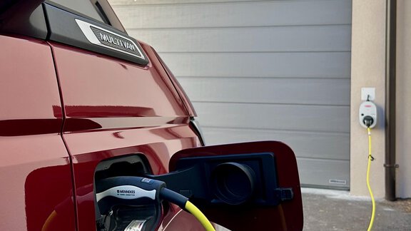 Ein rotes Elektroauto, das an einer Ladestation aufgeladen wird. Im Hintergrund ist eine Garage zu sehen. - ALPsmart - Oetz