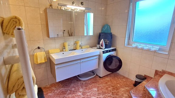 A modern bathroom with a double sink arrangement and a window. There is also a washing machine and a bathtub in the room. - Apart Annabell - Oetz